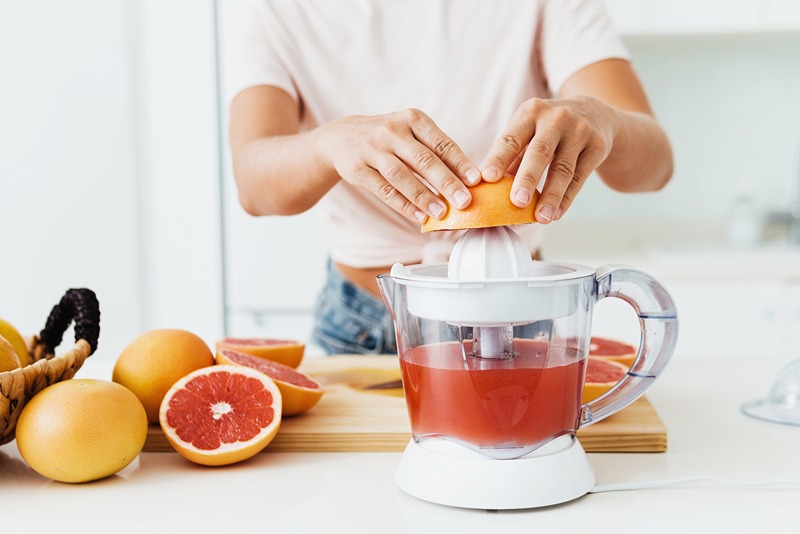Osoba si pripravuje ťavu z grapefruitu pomocou elektrickho odťavovača citrusov.
