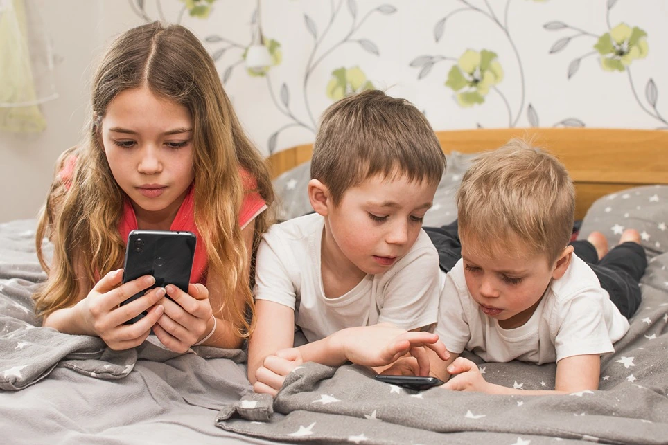 Deti a ich závislosť na mobile. Na obrázku sú deti zvalené na posteli s mobilom v ruke.