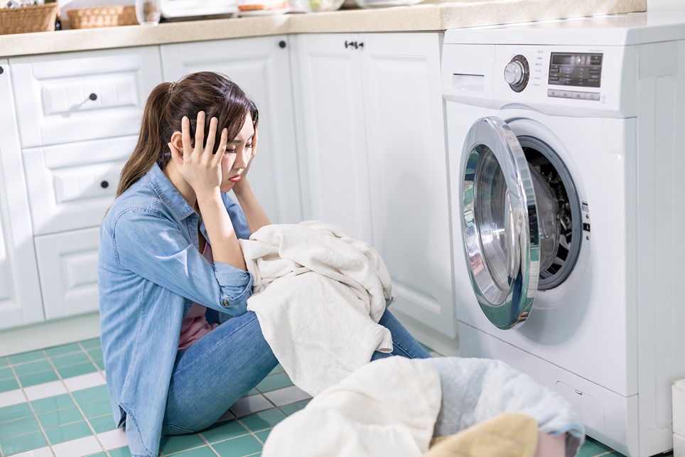 Na obrázku je frustrovaná žena, ktorá cíti zápach z práčky. 
