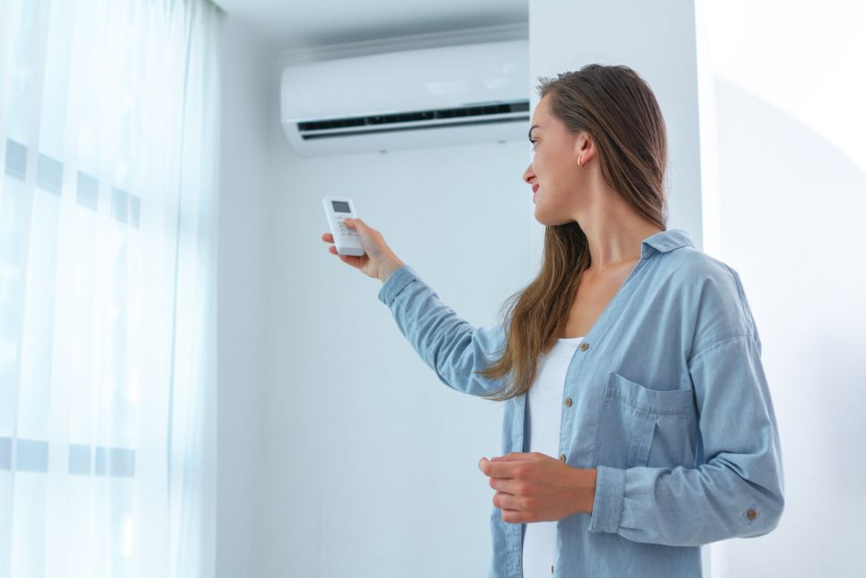 Žena si v byte zapína nástennú klimatizáciu